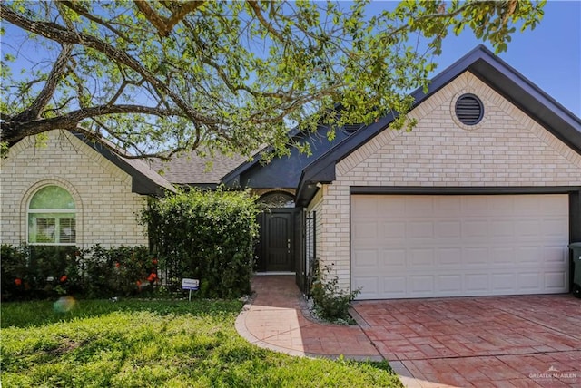view of front of property featuring brick siding, an attached garage, decorative driveway, and a front yard