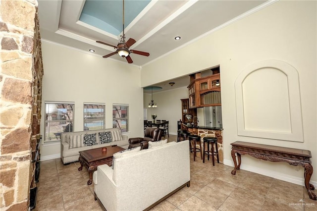 living room with a tray ceiling, a high ceiling, a ceiling fan, ornamental molding, and light tile patterned flooring