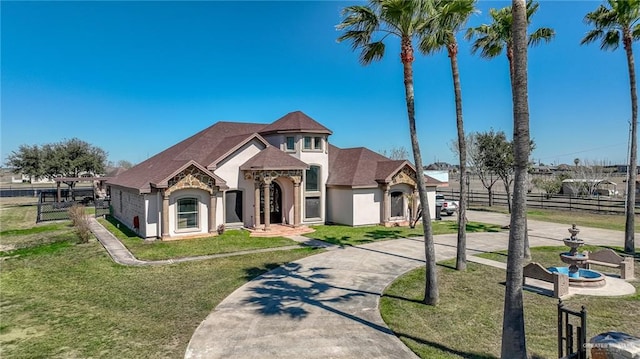 french country home featuring fence, stone siding, concrete driveway, stucco siding, and a front yard