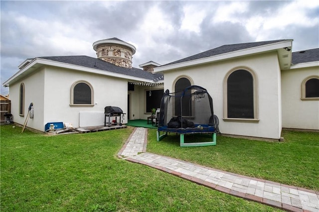 rear view of property featuring a lawn and a trampoline