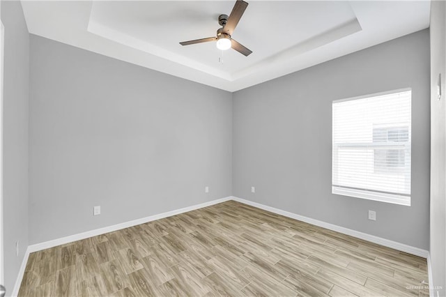 empty room featuring a tray ceiling, ceiling fan, and light wood-type flooring