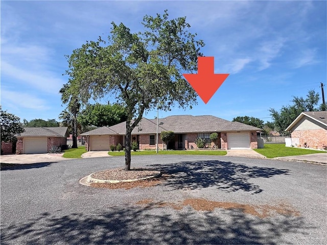ranch-style home with a front yard, brick siding, curved driveway, fence, and an attached garage