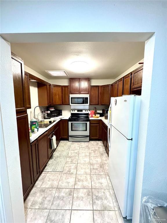 kitchen with stainless steel electric range oven, light countertops, light tile patterned floors, freestanding refrigerator, and a sink