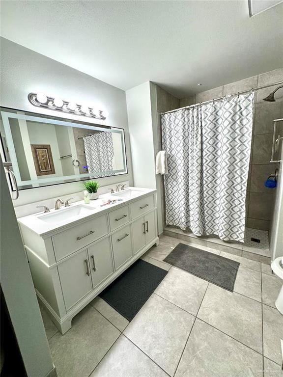 full bath with a sink, tiled shower, double vanity, and tile patterned flooring