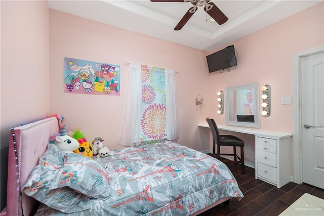 bedroom with ceiling fan, dark hardwood / wood-style floors, and a tray ceiling