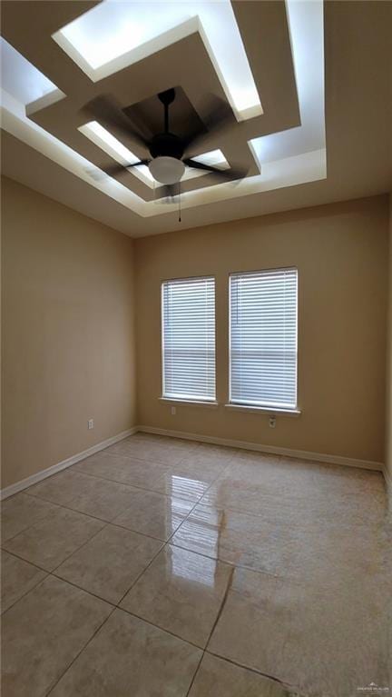 tiled empty room featuring a tray ceiling and ceiling fan