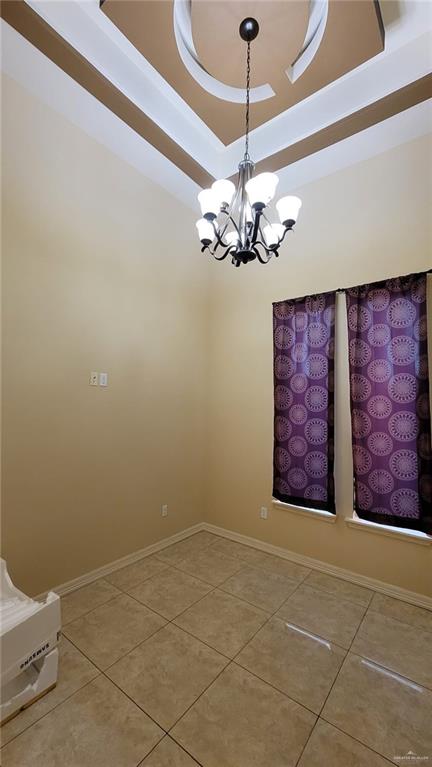 empty room with a chandelier, tile patterned floors, and a raised ceiling