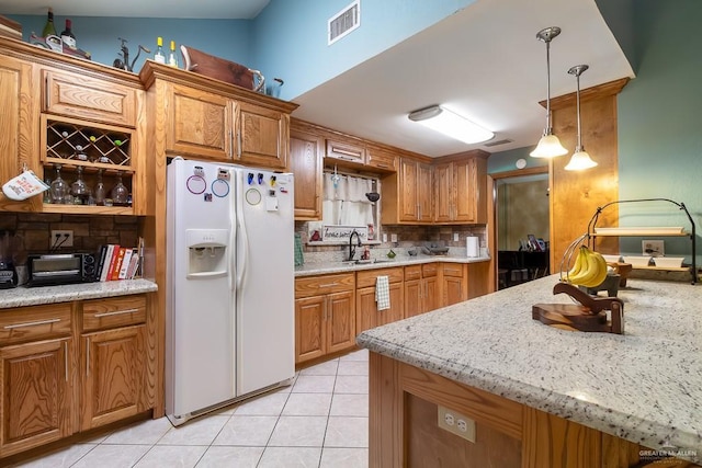 kitchen with white refrigerator with ice dispenser, a sink, brown cabinetry, decorative light fixtures, and light tile patterned floors