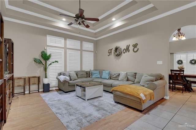 living room with ceiling fan with notable chandelier, light hardwood / wood-style flooring, and a raised ceiling