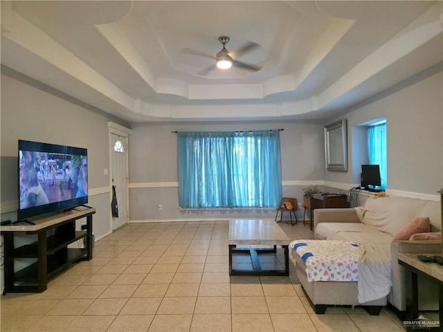 living area with a tray ceiling, light tile patterned flooring, and ceiling fan