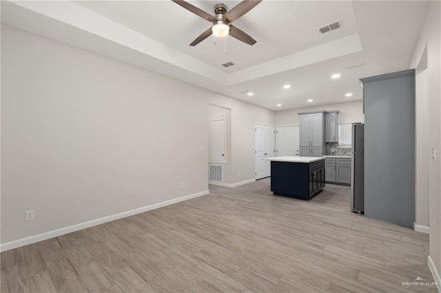 kitchen with decorative backsplash, light hardwood / wood-style floors, gray cabinets, a kitchen island, and stainless steel refrigerator