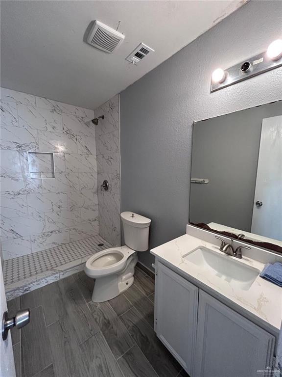 full bath featuring visible vents, tiled shower, vanity, and toilet