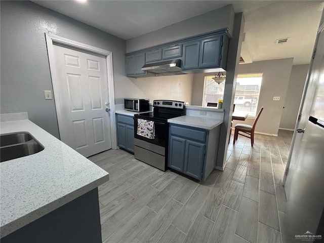 kitchen with wood finish floors, blue cabinetry, appliances with stainless steel finishes, a sink, and under cabinet range hood