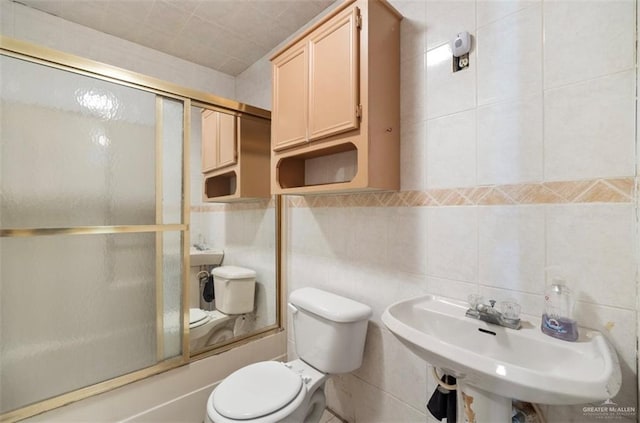 full bathroom with toilet, sink, enclosed tub / shower combo, and tile walls