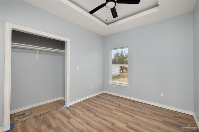 unfurnished bedroom featuring a closet, a raised ceiling, ceiling fan, wood finished floors, and baseboards