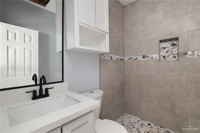 full bathroom with toilet, a tile shower, and vanity