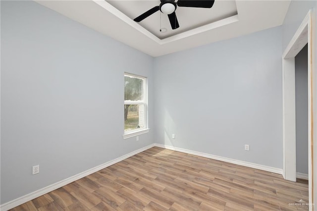 spare room with baseboards, a tray ceiling, ceiling fan, and wood finished floors