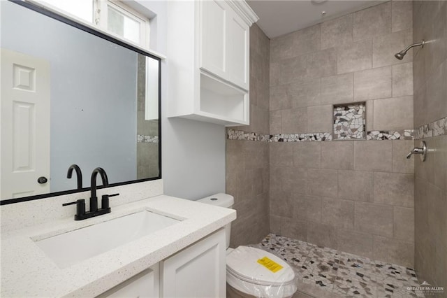 bathroom with toilet, a tile shower, and vanity