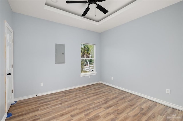 unfurnished room featuring a tray ceiling, light wood-style flooring, ceiling fan, electric panel, and baseboards