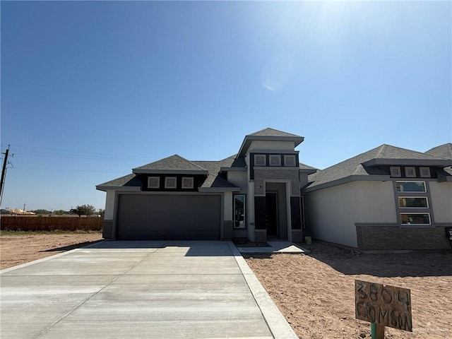 prairie-style home with stucco siding, stone siding, concrete driveway, and an attached garage