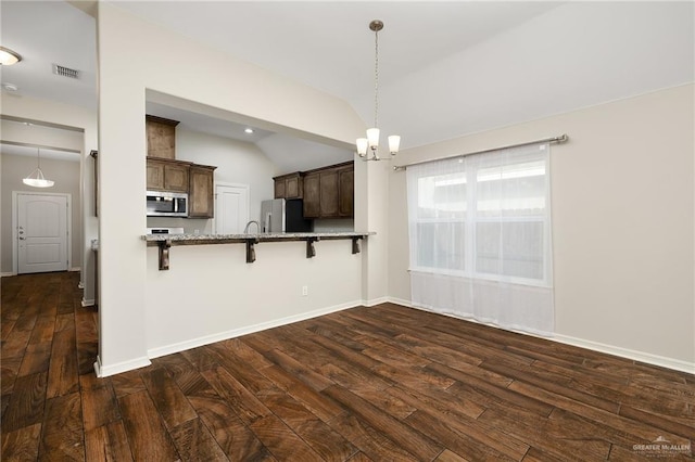 kitchen with vaulted ceiling, appliances with stainless steel finishes, a breakfast bar, pendant lighting, and kitchen peninsula