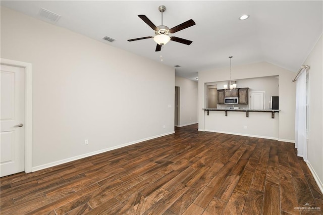 unfurnished living room with ceiling fan with notable chandelier, dark wood-type flooring, and vaulted ceiling