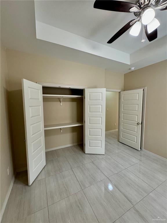 unfurnished bedroom featuring light tile patterned flooring, a closet, a ceiling fan, and baseboards