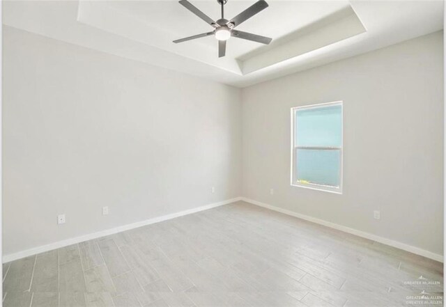 empty room featuring a tray ceiling, ceiling fan, and light hardwood / wood-style flooring