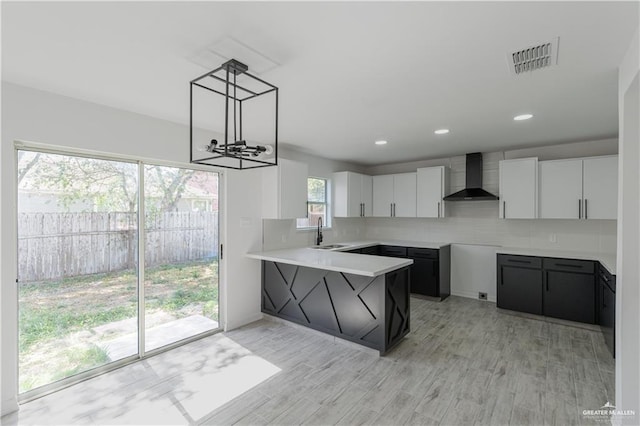 kitchen with a peninsula, wall chimney range hood, visible vents, a sink, and a notable chandelier