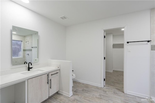 bathroom featuring tiled shower, vanity, visible vents, toilet, and wood finished floors