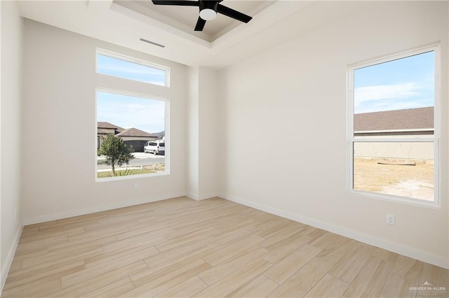 unfurnished room with light wood-type flooring, a tray ceiling, a wealth of natural light, and ceiling fan