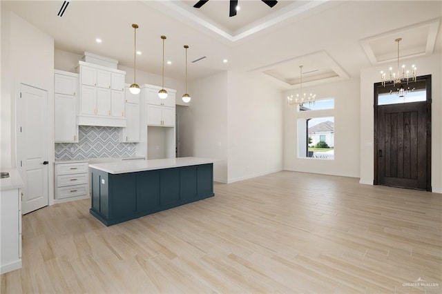 kitchen with a kitchen island with sink, white cabinets, ceiling fan with notable chandelier, a raised ceiling, and light hardwood / wood-style floors