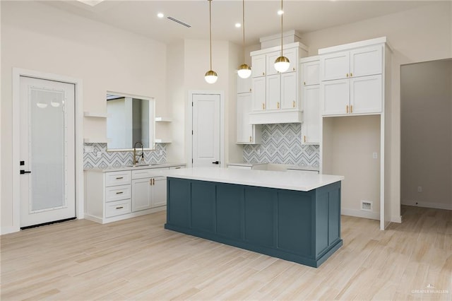 kitchen with white cabinetry, a kitchen island, hanging light fixtures, and light wood-type flooring