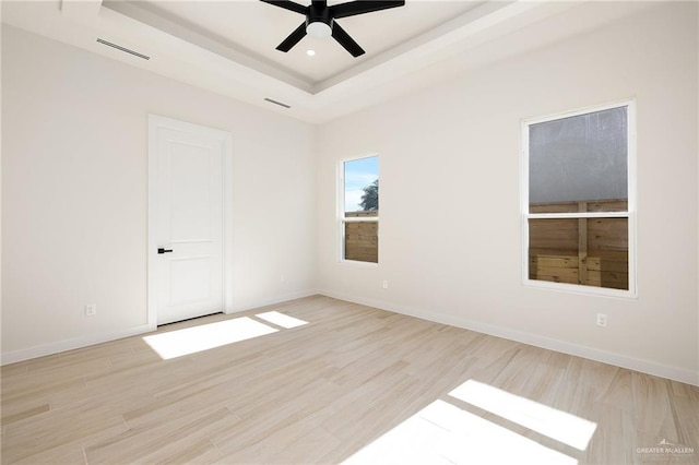 spare room with ceiling fan, light hardwood / wood-style floors, and a tray ceiling