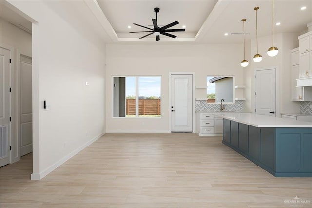 kitchen with white cabinetry, ceiling fan, tasteful backsplash, decorative light fixtures, and a tray ceiling