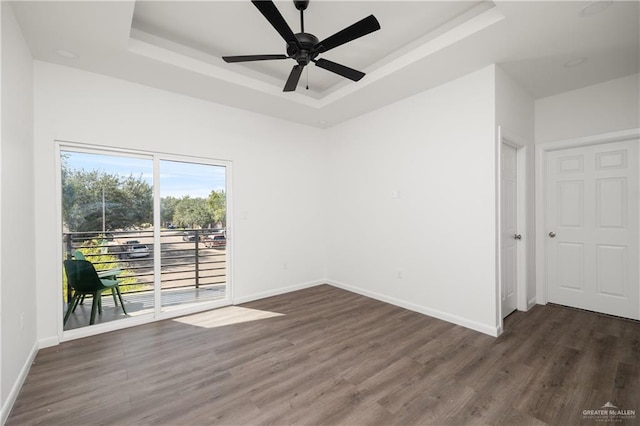 spare room featuring a tray ceiling, ceiling fan, and dark wood-type flooring