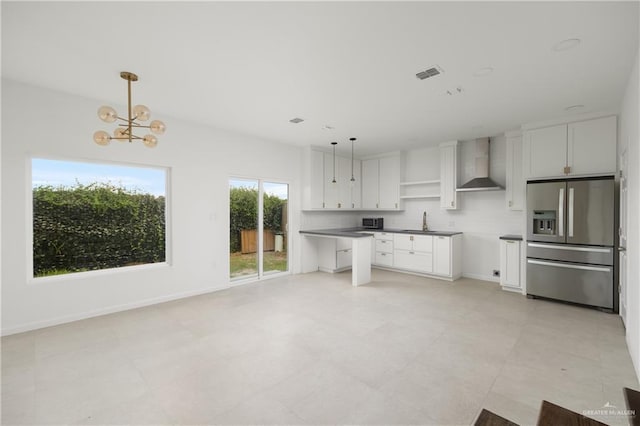 kitchen with white cabinets, wall chimney exhaust hood, stainless steel refrigerator with ice dispenser, and hanging light fixtures