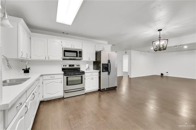 kitchen with appliances with stainless steel finishes, pendant lighting, white cabinetry, sink, and a chandelier