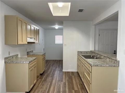 kitchen with dark wood-type flooring, exhaust hood, sink, light stone countertops, and light brown cabinetry