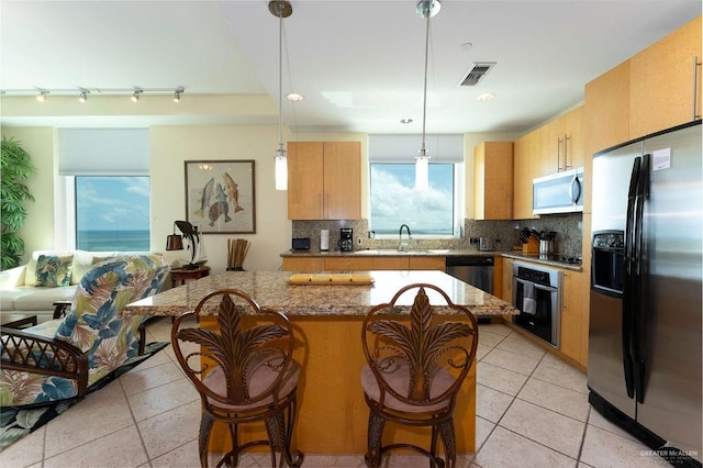 kitchen featuring decorative backsplash, appliances with stainless steel finishes, light stone counters, and pendant lighting