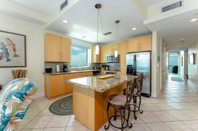 kitchen featuring appliances with stainless steel finishes, light stone counters, sink, decorative light fixtures, and a center island