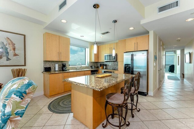 kitchen featuring appliances with stainless steel finishes, light stone counters, sink, decorative light fixtures, and a center island