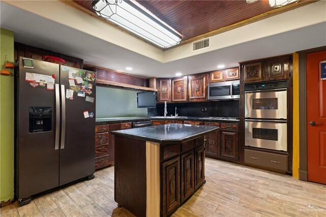 kitchen featuring visible vents, a sink, appliances with stainless steel finishes, dark countertops, and a kitchen island