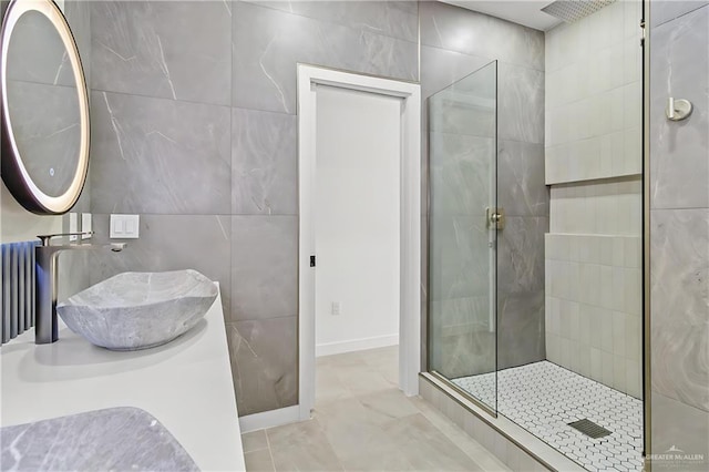 bathroom with tiled shower, tile patterned flooring, sink, and tile walls