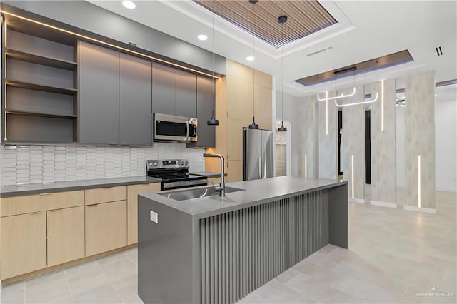 kitchen with sink, hanging light fixtures, stainless steel appliances, a tray ceiling, and an island with sink