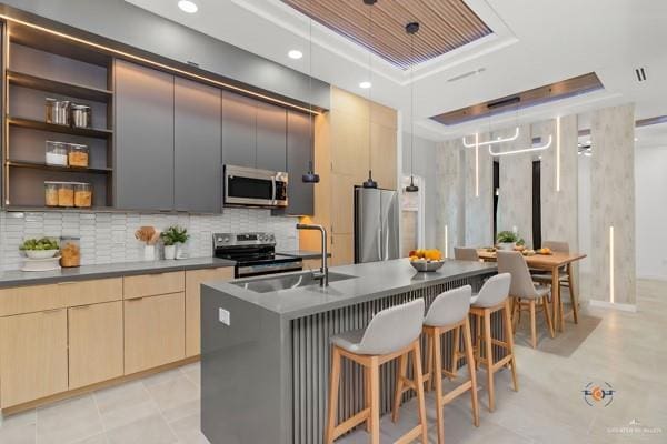 kitchen featuring sink, appliances with stainless steel finishes, a center island with sink, a tray ceiling, and a kitchen bar