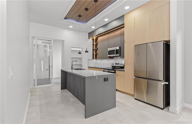 kitchen featuring appliances with stainless steel finishes, light brown cabinetry, sink, hanging light fixtures, and a kitchen island with sink