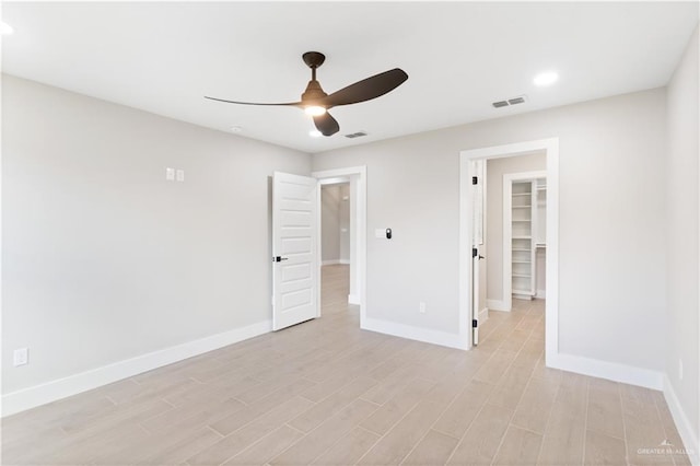 unfurnished bedroom with light wood-type flooring, a closet, a spacious closet, and ceiling fan