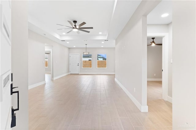 unfurnished living room with light hardwood / wood-style floors, ceiling fan, and a tray ceiling