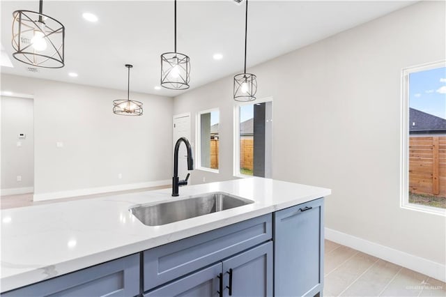 kitchen with decorative light fixtures, light wood-type flooring, light stone countertops, and sink